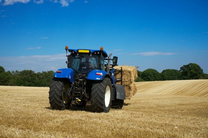 tractor paie cereale pexels-mikebirdy-12973137 Un tractor de culoare albastra transporta balorti de paie dupa recoltarea cerealelor de pe un cam agricol