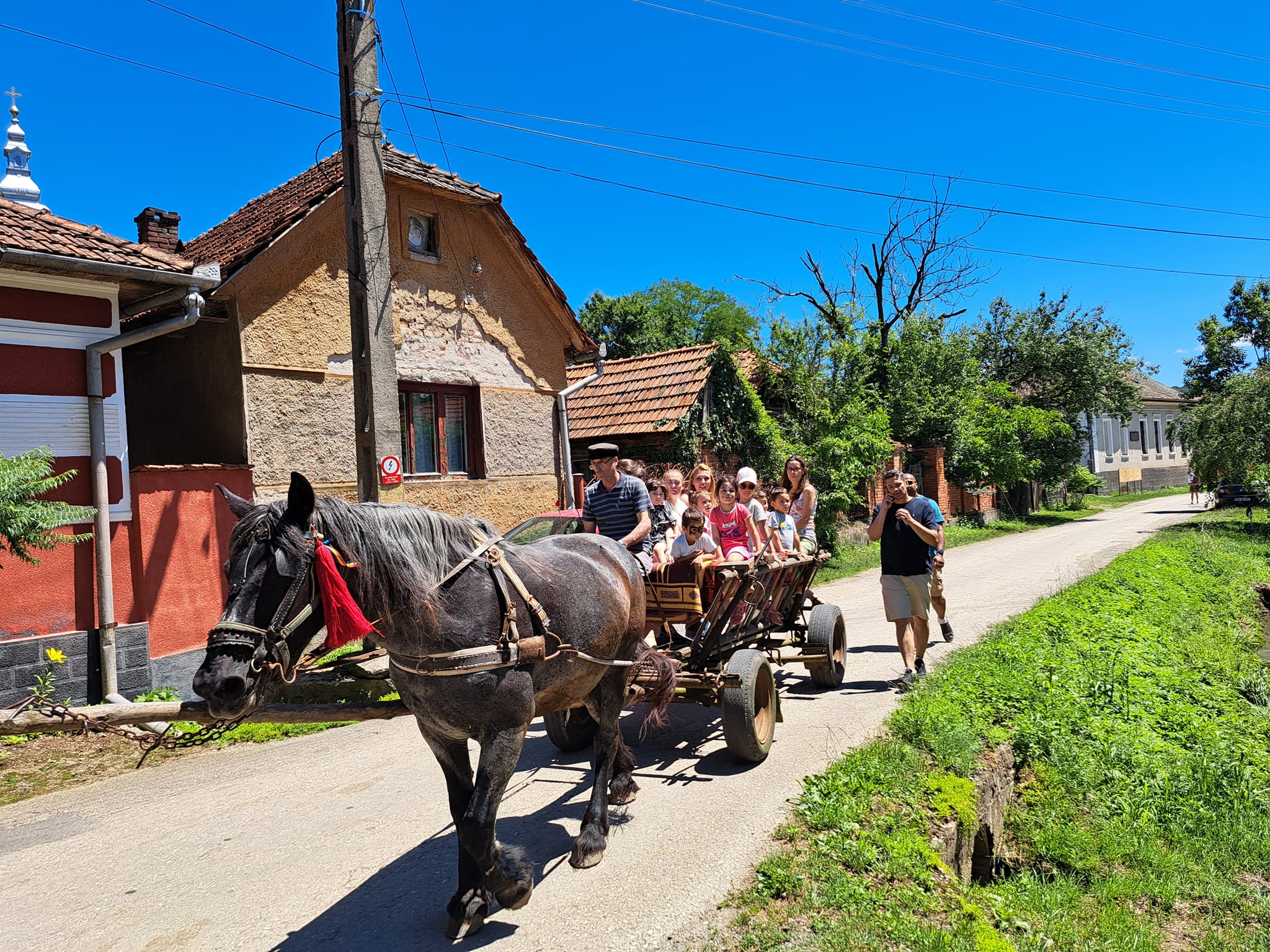 Grup de turiști, adulți și copii, într-o căruță trasă de cai pe o uliță din satul Margina, județul Timiș.