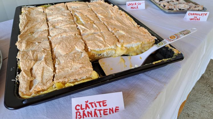 O tavă mare cu clătite bănățene acoperite cu un strat generos de bezea, flancată de farfurii cu lașce cu nucă și cornulețe cu untură.
